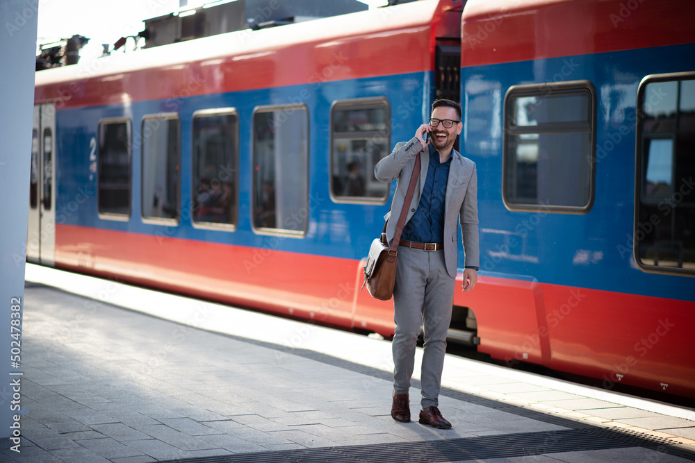 Young businessman on train station, walking and talking on phone