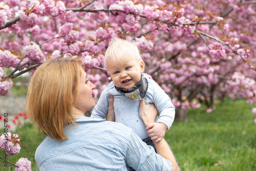 happy woman with little baby boy near pink sakura blooming tree. Spring concept