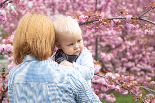 Beautiful woman with little baby boy near pink sakura blooming tree. Spring concept
