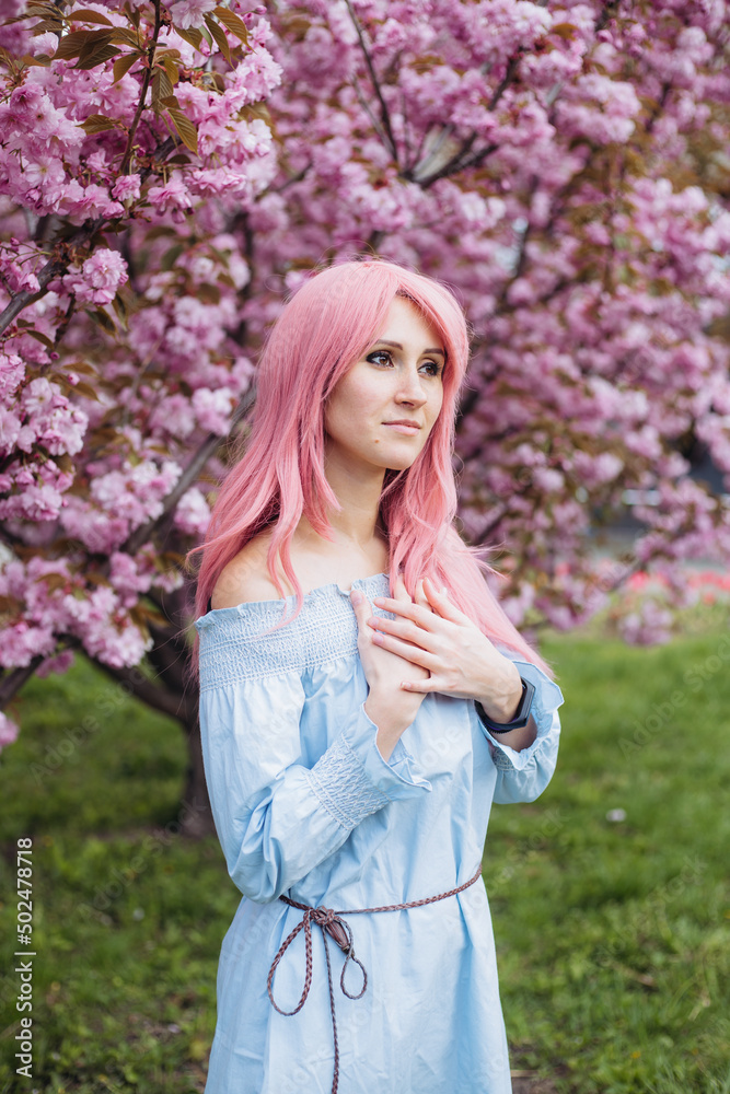 Young beautiful woman near sakura blooming tree. Pink flowers, spring and youth concept. Stylish girl smiling. Blooming garden with cherry-tree. Copyplace, place for text. Young beautiful woman near sakura blooming tree. Pink flowers, spring and youth concept. Stylish girl smiling. Blooming garden with cherry-tree. Copyplace, place for text.