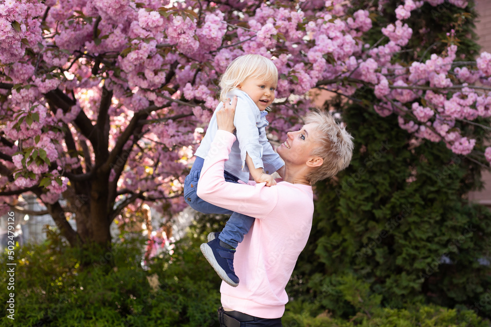 Obraz premium Little boy and mother have a good time on weekend activity in the blooming Sakura gardens. Mom and little son in nature playing at spring park.
