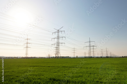 A lot of high-voltage power line, transmission tower overhead line masts, high voltage pylons also known as power pylons on the fields with grain. 