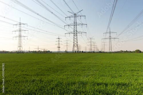 A lot of high-voltage power line, transmission tower overhead line masts, high voltage pylons also known as power pylons on the fields with grain. 