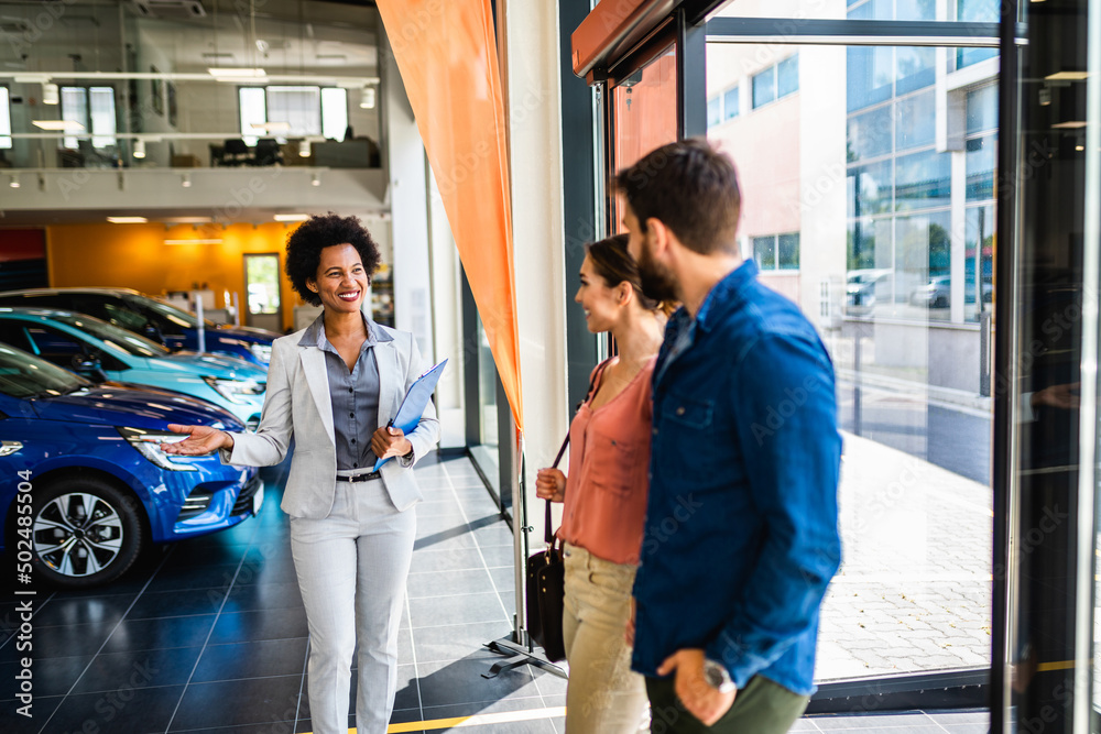 Young couple talking with saleswoman at car showroom about new car they want to buy. Young couple talking with saleswoman at car showroom about new car they want to buy.