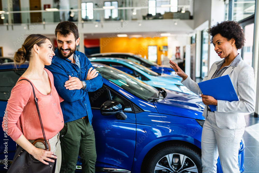 Young couple talking with saleswoman at car showroom about new car they want to buy.