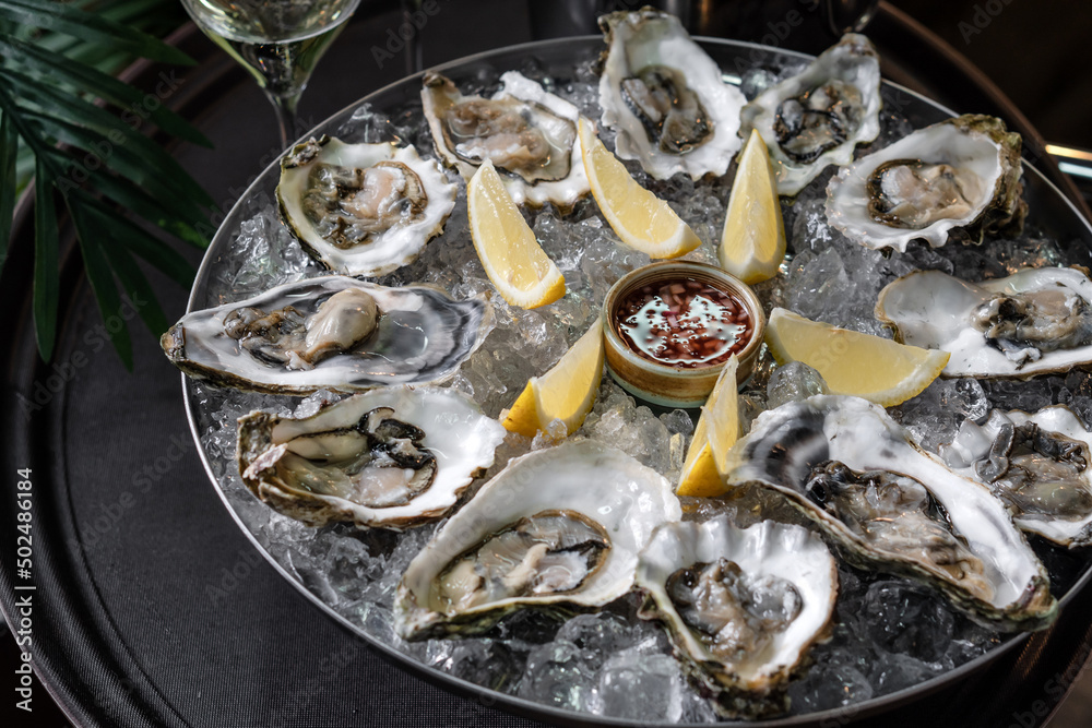 Fresh oysters on a platter in ice with a slice of lemon and spicy sauce. Fresh oysters on a platter in ice with a slice of lemon and spicy sauce.