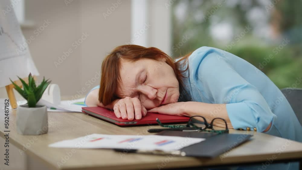 Side view tired mature woman sighing taking a nap sitting at table in office. Portrait of sad exhausted Caucasian businesswoman putting head on table closing eyes. Tiredness and exhaustion Side view tired mature woman sighing taking a nap sitting at table in office. Portrait of sad exhausted Caucasian businesswoman putting head on table closing eyes. Tiredness and exhaustion