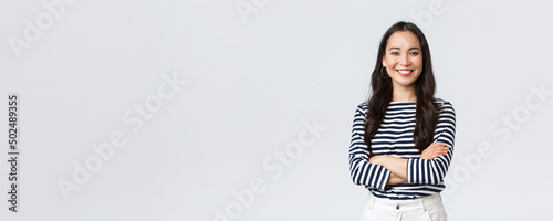 Lifestyle, beauty and fashion, people emotions concept. Young asian female office manager, CEO with pleased expression standing over white background, smiling with arms crossed over chest