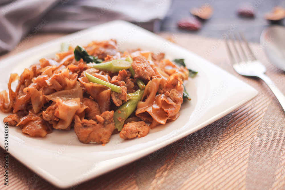 Stir fried Noodle with black soy sauce served in a white plate. on the black wooden table or what we call Stir fried Noodle with black soy sauce served in a white plate. on the black wooden table or what we call