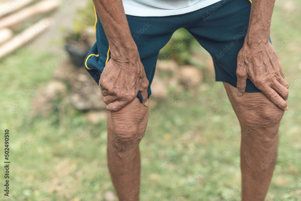 An anonymous thin old man clutches his knees while feeling