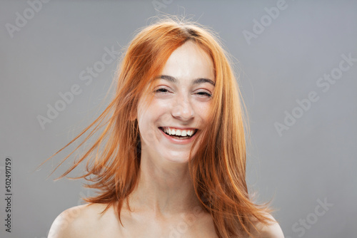Beautiful dark burnt orange windy hair girl smiling. Studio portrait with happy face expression against gray background...