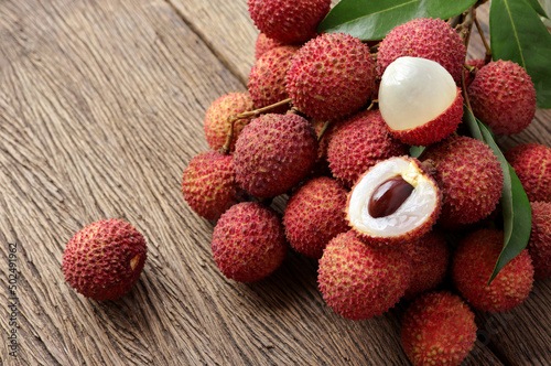 Fresh ripe lychee fruit and peeled lychee with green leaves on wooden background. rustic style, from above