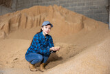 Woman agronomist squatting at bunch of soybean husk inside of fodder storage.