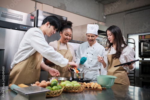 Hobby cuisine course, senior male chef in cook uniform teaches young cooking class students to prepare, mix and stir ingredients for pastry foods, fruit pies in restaurant stainless steel kitchen.