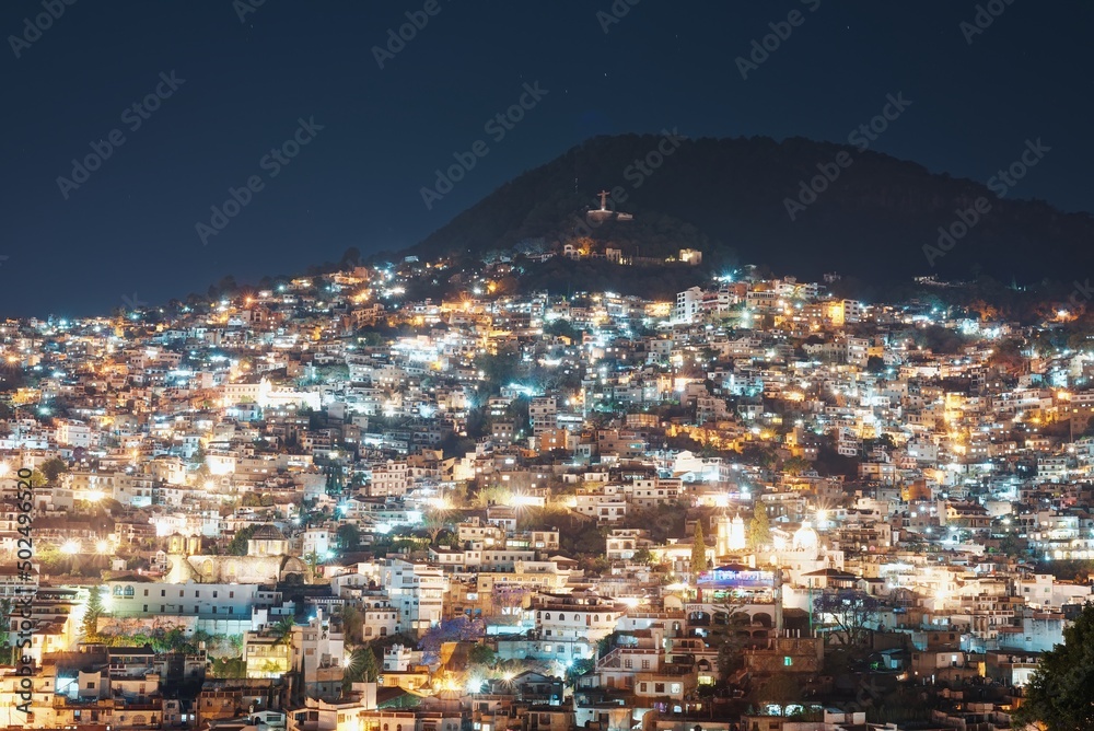 Lights of the night city on the slope of the mountain. The light of lanterns and windows of houses with colonial architecture. Dark blue night sky. Narrow streets of Taxco in Mexico