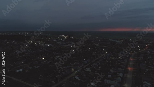 Aerial view of night Village. Lightning flashes on the sky, a thunderstorm begins. Around you can see houses, forests and fields. The lights are on, the cars are driving on the roads
