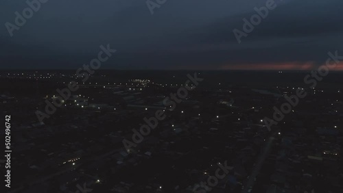 Aerial view of night Village. Lightning flashes on the sky, a thunderstorm begins. Around you can see houses, forests and fields. The lights are on, the cars are driving on the roads
