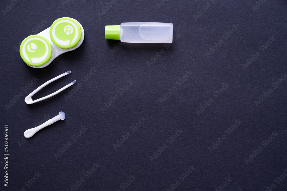 Container with contact lenses, tweezers, suction cup and bottle with solution on dark blue background, top view, copy space Container with contact lenses, tweezers, suction cup and bottle with solution on dark blue background, top view, copy space
