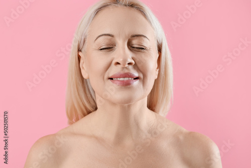 Mature blonde woman with healthy skin on pink background, closeup