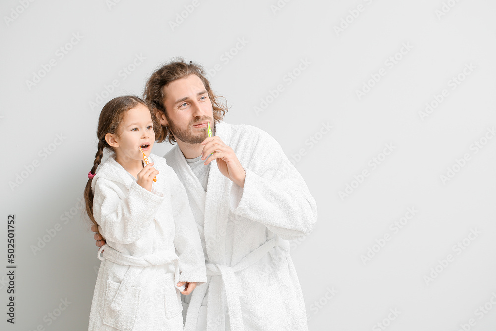 Little girl with her father brushing teeth on light background Little girl with her father brushing teeth on light background