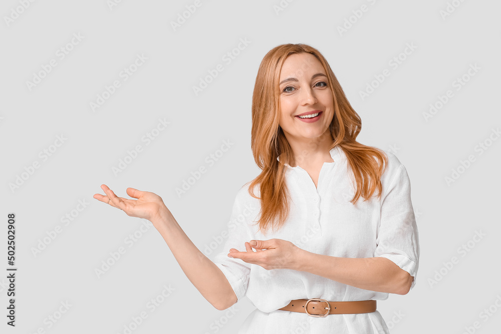 Mature woman showing something on grey background Mature woman showing something on grey background