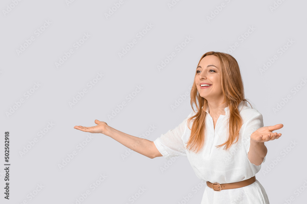 Happy mature woman opening arms for hug on grey background Happy mature woman opening arms for hug on grey background