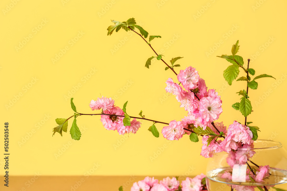 Fototapeta premium Vase with blooming branches on table near yellow wall