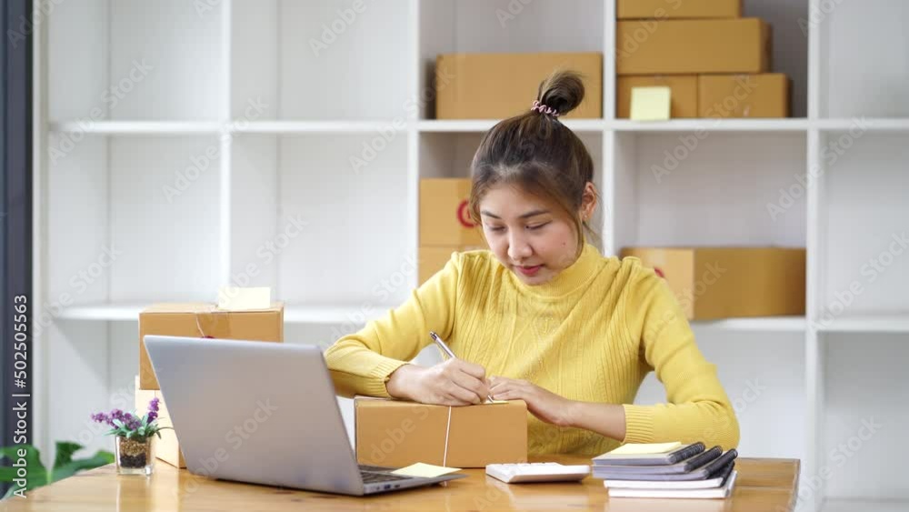 Happy young Asian business owner woman prepare parcel box and check online orders of product for deliver to customer on laptop computer. Shopping Online concept. Happy young Asian business owner woman prepare parcel box and check online orders of product for deliver to customer on laptop computer. Shopping Online concept.
