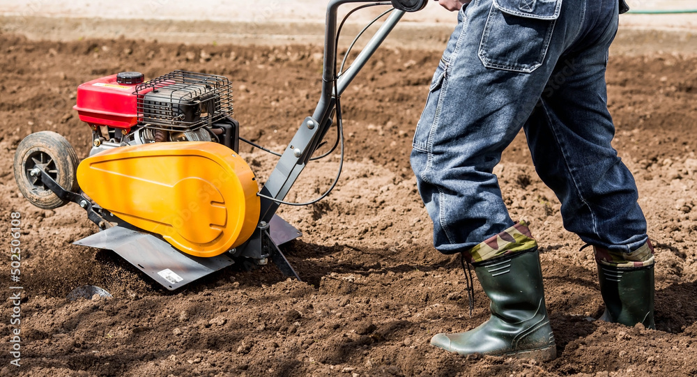 Fototapeta premium Banner. A male farmer plows the land with a cultivator. Agricultural machinery for tillage in the garden, combine harvester.