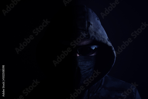 Stylish man in dark hoodie with black glasses and mask dark background, hacker, attacker and bandit.