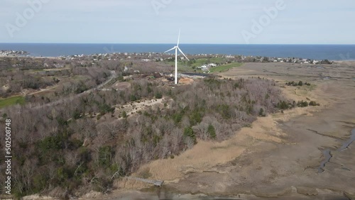 Aerial push over water toward wind turbine on the edge of Scituate Driftway marshes. Atlantic Ocean in the distance. photo