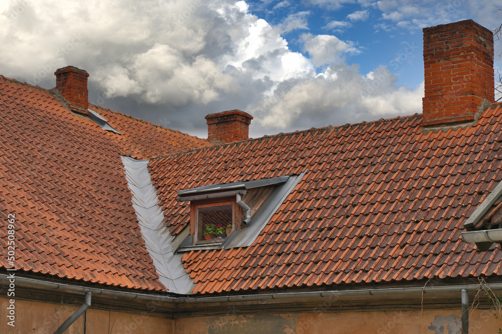 Red tiled roof of a residential building with a dormer window.