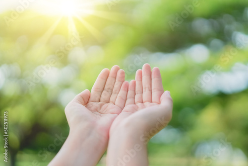 Woman open hand up to sunset sky and green blur leaf bokeh sun light abstract background.