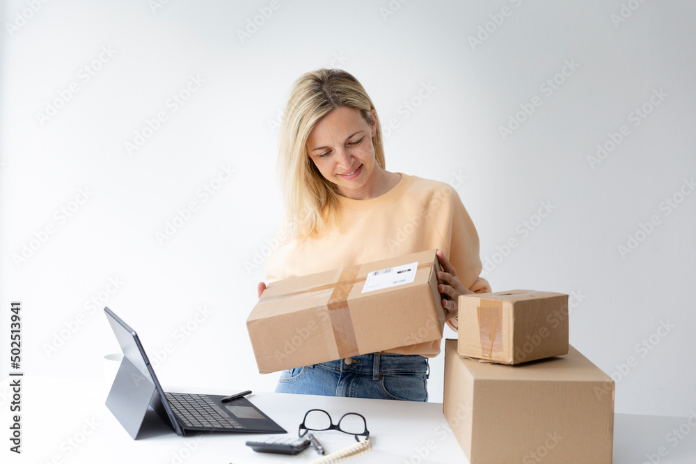 pretty young woman standing by height adjustable table looking at various parcels she has ordered or is about to ship via internet pretty young woman standing by height adjustable table looking at various parcels she has ordered or is about to ship via internet