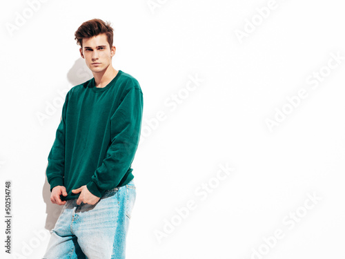 Portrait of handsome confident stylish hipster lambersexual model.Man dressed in green sweater and jeans. Fashion male posing in studio near white wall. Isolated