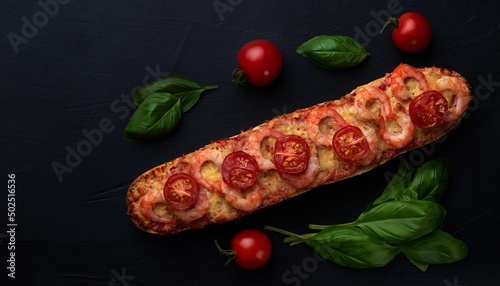 Homemade baguette sandwich or pizza with shrimp, cherry tomatoes on top. Top view photo on a dark background with place for your text.