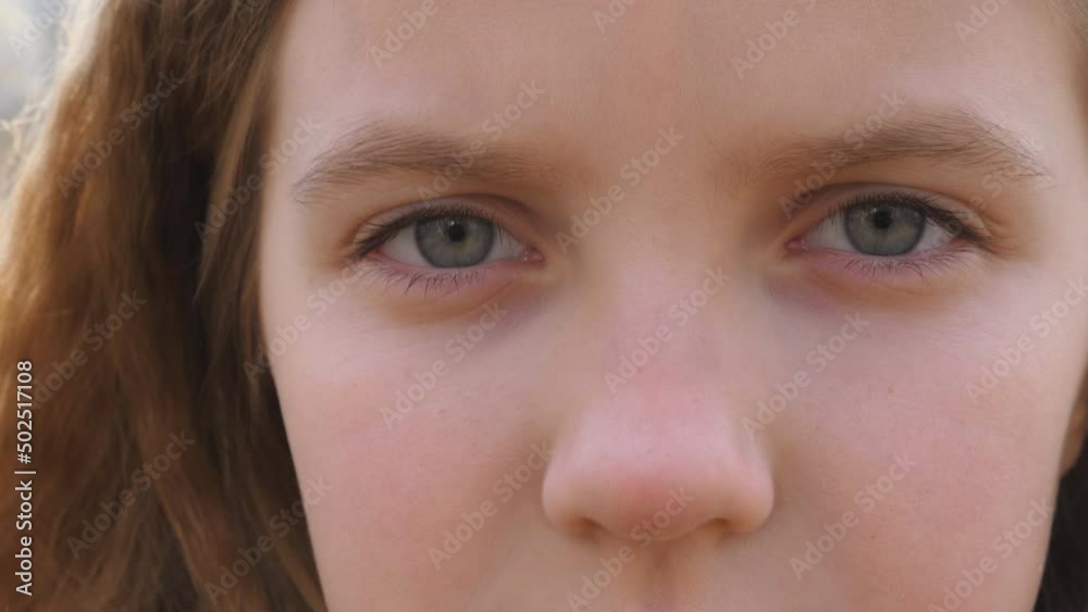 Close up blue eyes of unhappy little blonde girl blinking and looking into camera with a