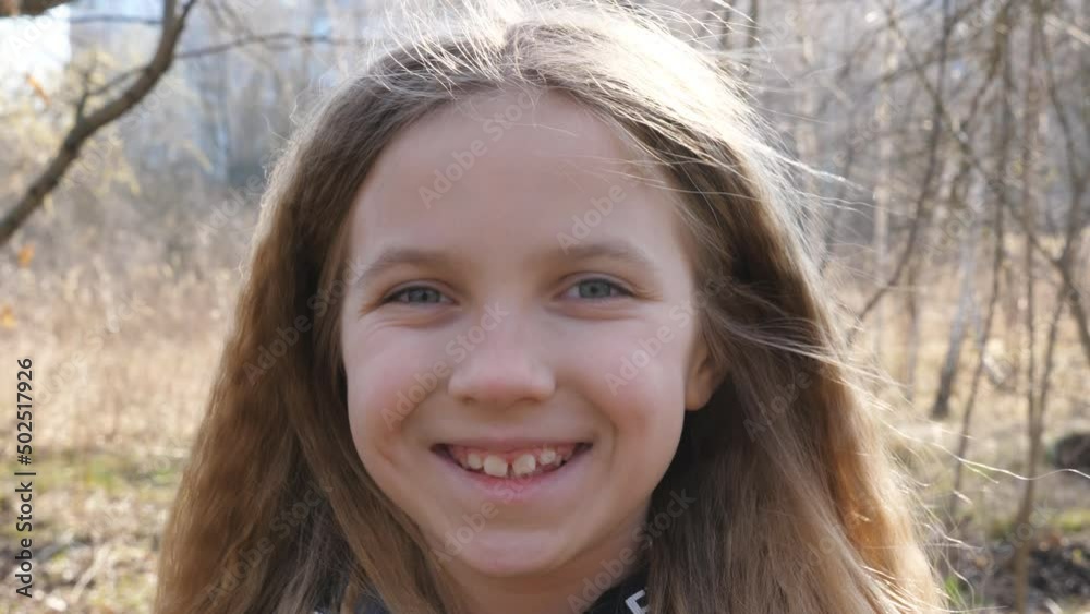 Portrait of happy small child against the blurred background of a forest in early spring. Smiling blonde girl looking into camera outdoor. Close up emotions of female kid with glad expression on face Portrait of happy small child against the blurred background of a forest in early spring. Smiling blonde girl looking into camera outdoor. Close up emotions of female kid with glad expression on face