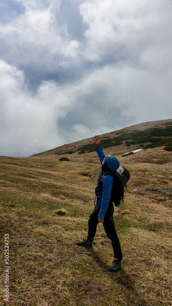 Man with backpack on scenic hiking trail asking for weather change in cloud covered mountain peaks of the Hochschwab Region, Upper Styria, Austria. Alpine meadows in Alps, Europe. Talking to god. Rain