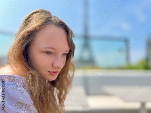 tender face of a girl with freckles close-up she has blond hair and bright eyes She looks and can be used for any advertisement there is a place for text. Eiffel Tower in the background