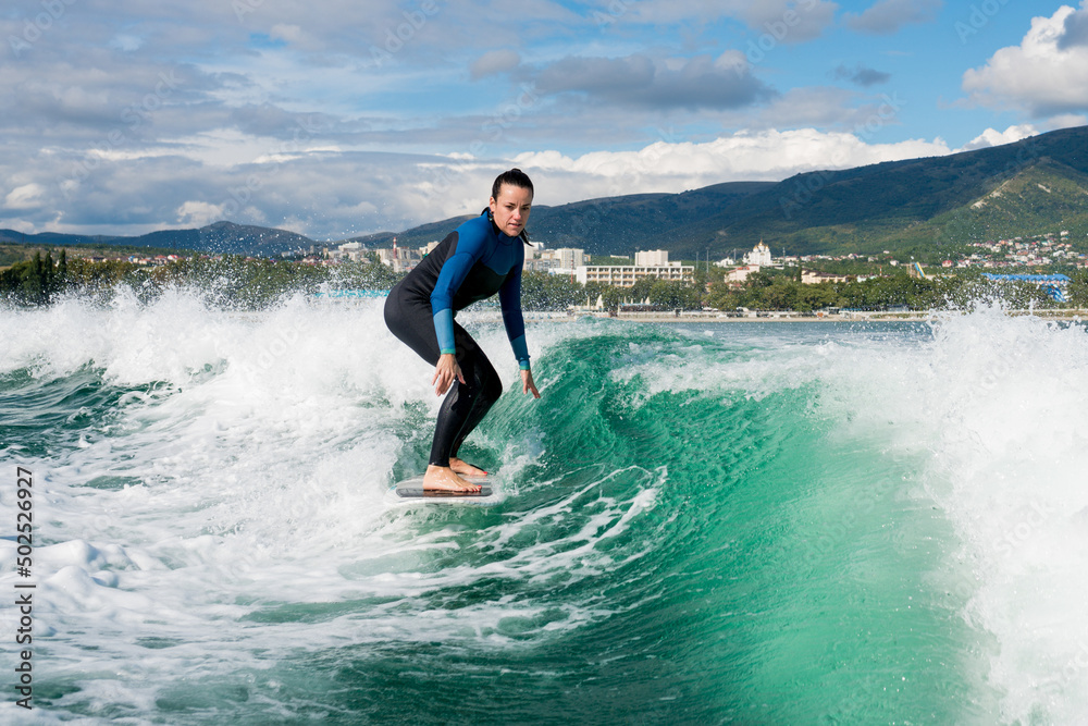 Wakesurfing. Young woman in wetsuit learning to wakesurf on the sea. Athletic female riding the waves on sunny day. Watersport concept. Wakesurfing. Young woman in wetsuit learning to wakesurf on the sea. Athletic female riding the waves on sunny day. Watersport concept.