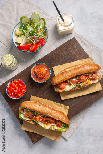 Banh Mi - Vietnamese sandwich with sausage, pork, lettuce, tomato and arugula on the light grey texture background. One of the most famous street food in the world