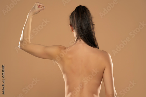 Canvas Print Back view of young nude woman with ponytail, showing arm on a beige background