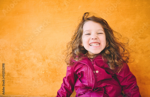 Young girl with a cheeky smile looking directly at the camera against a bright yellow wall background photo