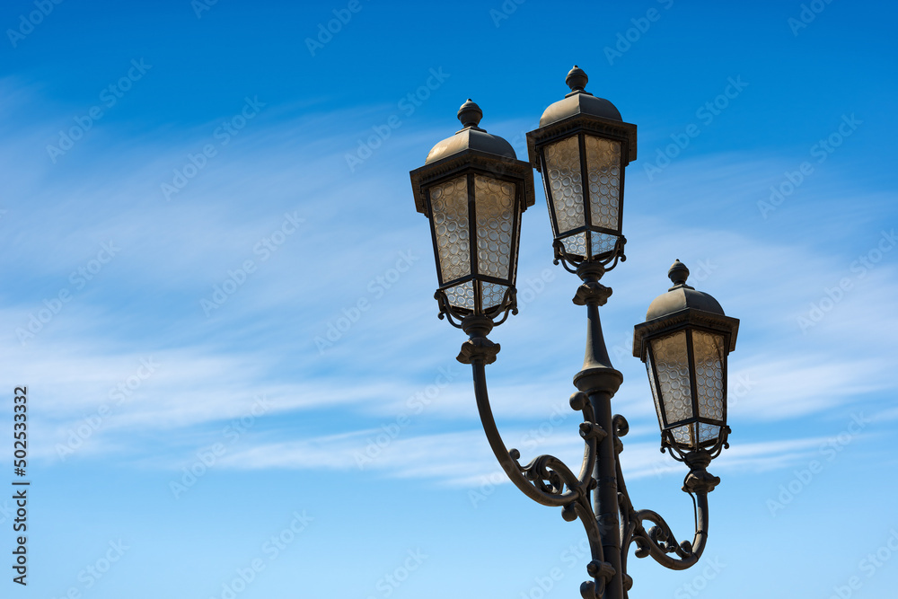 Close-up of old street lamp posts against a clear blue sky with clouds and copy space. Loggia town square (Piazza della Loggia), Brescia downtown, Lombardy, Italy, Southern Europe.