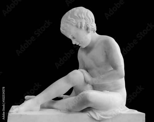 Ancient marble statue of a sitting boy. Young man sculpture isolated on black background. Antique stone monument