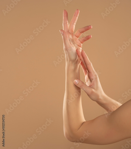Cropped shot of woman applying cosmetic product on her hands on a beige background. Young woman applying hand cream