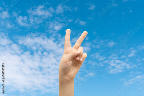 Peace sign gesture made by child on blue sky background. World peace concept.