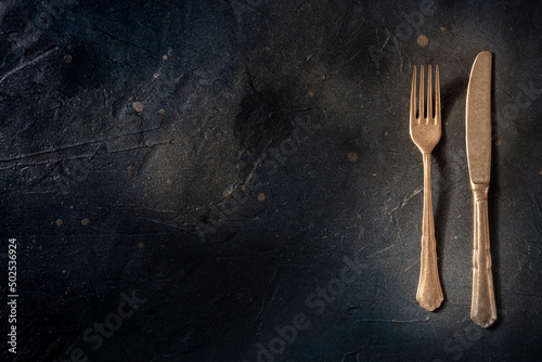 Cutlery. A fork and a knife on a black slate background. Modern tableware on a dark table with a place for text, overhead flat lay shot