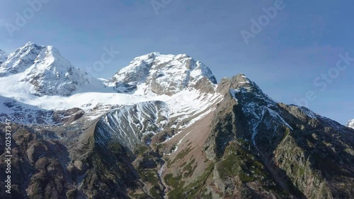 Drone flying along snow covered white mountain glacier in sunny autumn day, Tuymazinsky glacier, Digoriya gorge, Northern Ossetia - Alania, Caucasus, Russia